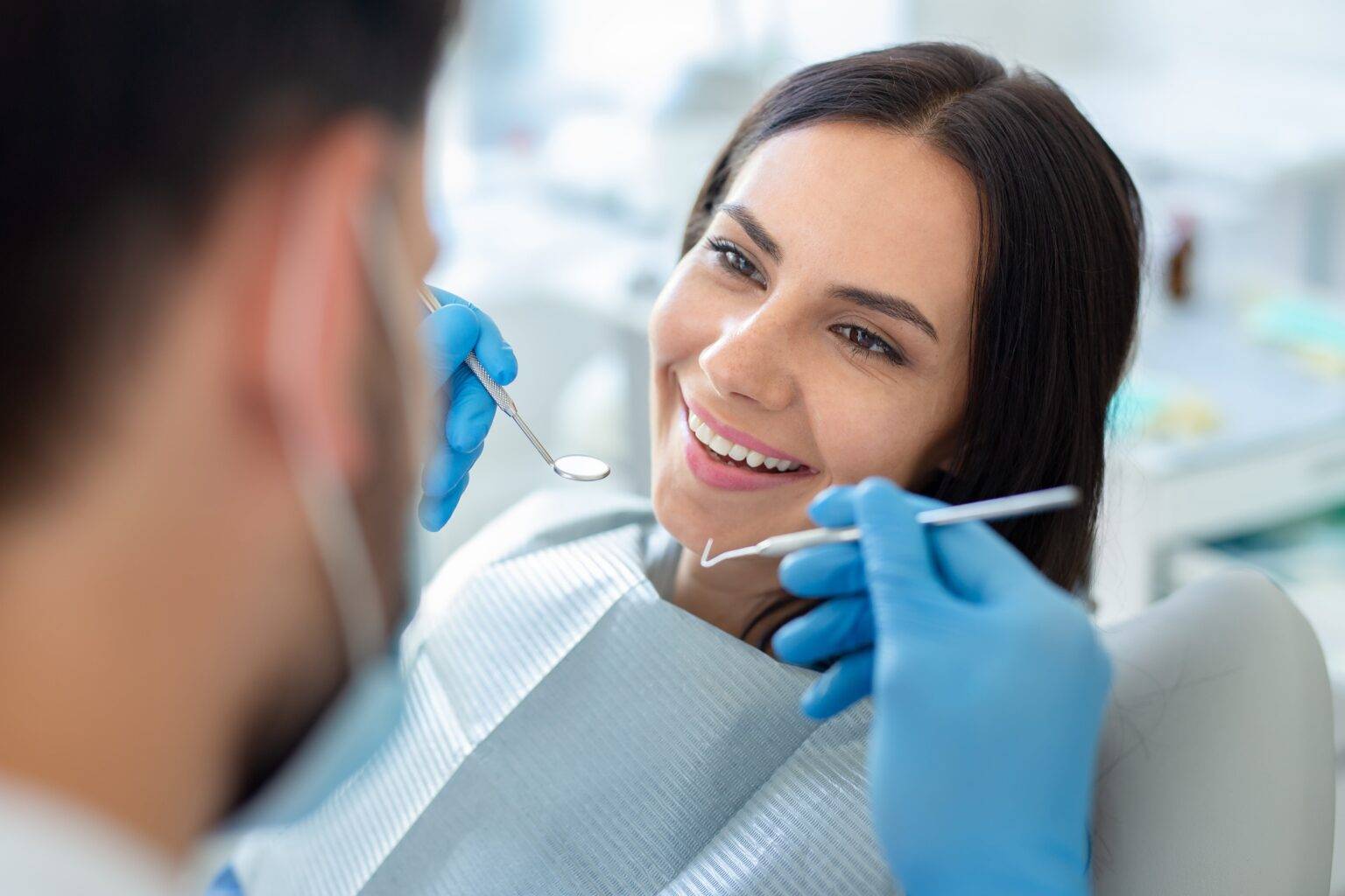 Una paziente sorridente durante una seduta di ablazione del tartaro in uno studio dentistico Confident, mentre il professionista utilizza specchietto e sonda per il controllo del cavo orale.